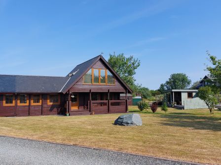 A wooden house with a lawn and trees at Eirianfa in Menai Bridge