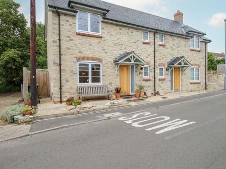 A stone house with wooden doors and windows along a road with slow painted on the street at Wren in Upwey