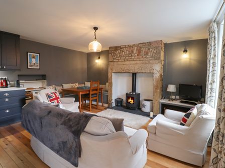 A living room with a wood burning stove dining table chairs and a sofa at Grebe Cottage in Alnmouth