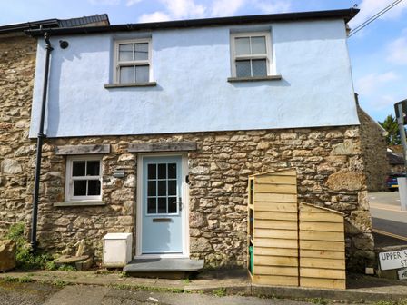 A stone house with a light blue door and windows and a wooden structure outside at Penpwmp in Newport Pembrokeshire