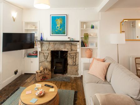 A living room with a stone fireplace a mounted television a gray sofa a wooden coffee table and built-in shelves at 11 Belgravia Street in Penzance