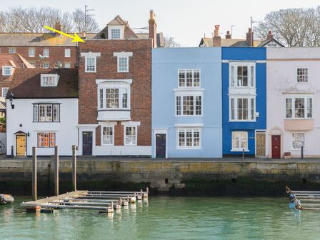 A row of colorful waterfront houses with windows and doors along a stone wall with wooden docks in front at Stanley House in Weymouth