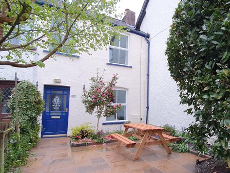 An outdoor patio with a wooden picnic table a blooming tree and a blue door at Bay Tree Cottage in Keswick