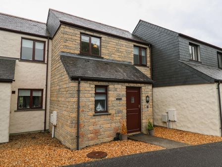 A stone front house with brown door and windows and gravel driveway at Alberts Den in Falmouth