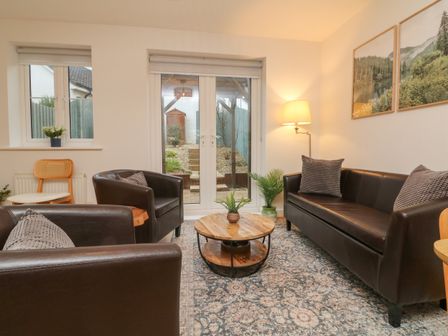 A living room with brown leather sofas a round wooden coffee table a floor lamp and two framed pictures at Reubens Cottage in Fremington Devon