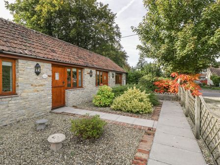 Stone cottage with wooden doors and windows and garden path with shrubs at The Paddock in Wookey near Wells