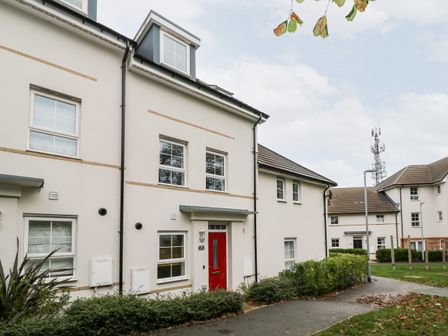 A street view of white residential buildings with red and blue doors and surrounding greenery at 20 Bishops Way in Falmouth