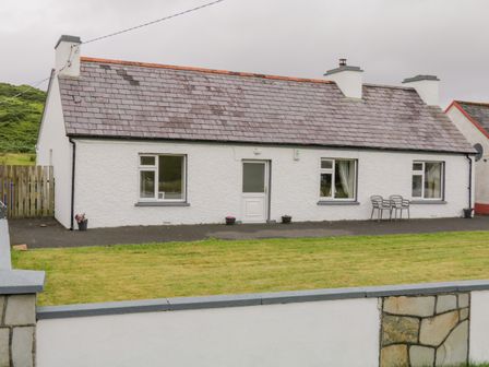 A white single-story house with three chimneys two chairs on the front and a lawn at Maghera Caves Cottage in Ardara County Donegal