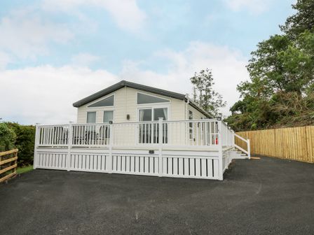 A single story house with white railing and gate with paved driveway and trees at Platinum Lodge in Borth