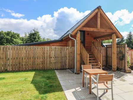 A wooden structure with stairs leading to an upper level and a table with two chairs on a tiled patio at Spicery Barn Loft in Tedburn St Mary