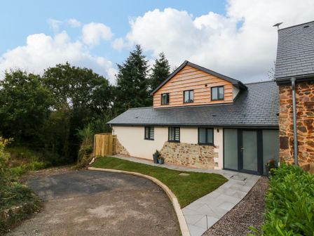 A house with stone and wood exterior walls surrounded by trees and a paved driveway at Spicery in Tedburn St Mary