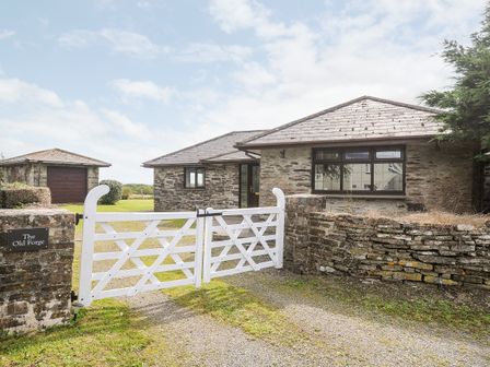 A stone house with a white wooden gate and a detached garage at The Old Forge in Trerulefoot