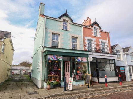A street view of a two-story building with shops on the ground floor and windows on the upper floors at The Bell Apartment in Cemaes Bay
