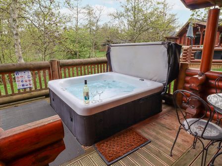 An outdoor hot tub with a bottle of wine and two glasses on the edge on a wooden deck with a metal chair at 24 Lakeside Drive in Felton