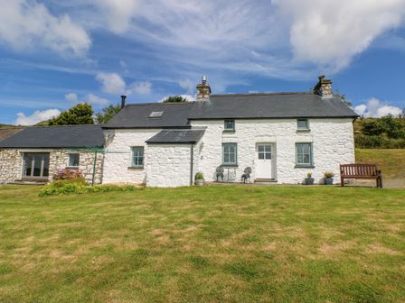 A white stone cottage with grey roof and green window frames with a grassy lawn in front at Bryn Nante Morvil near Maenclochog