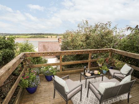 An outdoor wooden deck with seating area and table overlooking a river at 12 Brynffynnon in Y Felinheli
