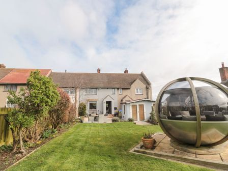 A backyard with a green lawn a patio with chairs a shed and a spherical outdoor pod at Coast Cottage in Bamburgh