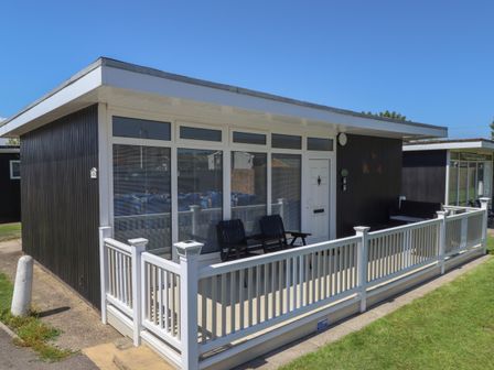 A small black and white cabin with a white fence and black chairs on the porch at 114 Cherry Park in Chapel St Leonards