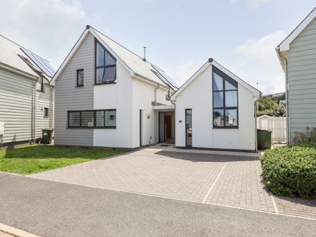 A modern detached house with triangular roofs and large windows with a driveway and lawn at Pebble Ridge View in Westward Ho