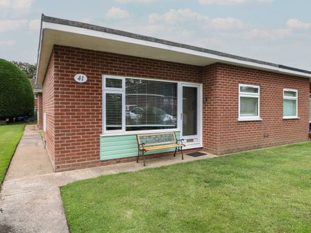 A single-story brick house with windows a bench by the door and a lawn at 41 Siesta Mar Chalet Park Mundesley
