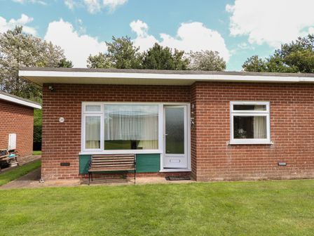 A one story brick house with two windows a door and a bench on a lawn at 31 Siesta Mar Chalet Park in Mundesley
