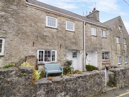 A stone house exterior with white windows blue and brown benches and a stone wall at 3 Moranedd in Moelfre