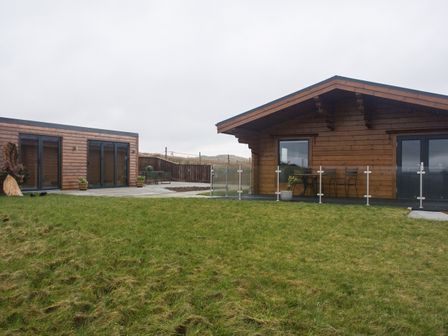 A yard with green grass in front of two wooden cabin buildings at Height End Farm Log Cabin Rossendale near Bacup