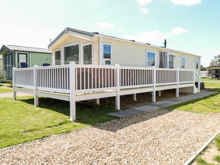 A mobile home with a white railing deck and gravel path outside at Hazell Thorne Hideaway in Fritton