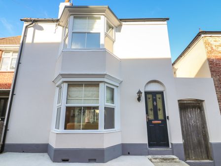 A white two-story house with bay windows and a dark front door at Bay Cottage in Weymouth