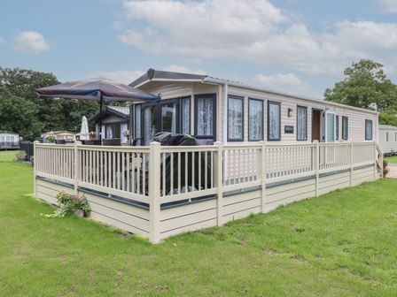 A mobile home with a fenced deck and outdoor furniture including an umbrella and grill at Stanley's Lodge Foxburrow Hang in Belton Norfolk