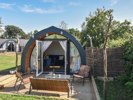 A garden with a wooden deck patio set in front of an arched cabin with glass doors at Cedar in Wootton Fitzpaine near Charmouth