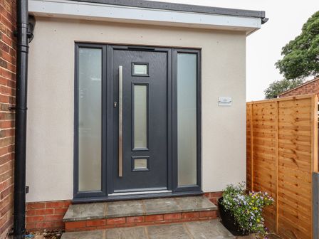 A front door with frosted glass panels and a flower pot beside a wooden fence at The Woodpecker in Scarborough