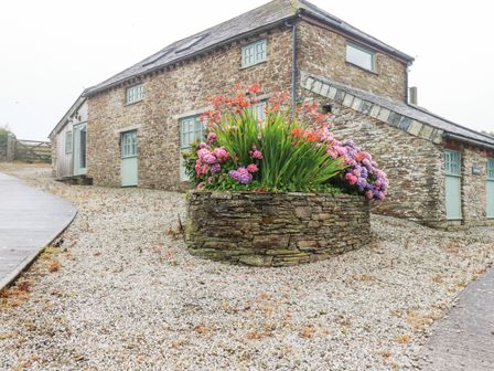 A stone house with green window frames and a stone planter with colorful flowers in front at Trerubies in Delabole