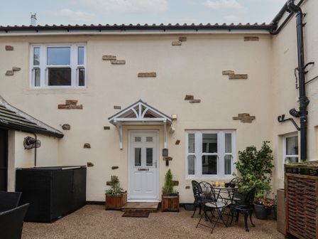 A courtyard with a white door and windows black metal table and chairs and plants at Hideaway Cottage in Whitby