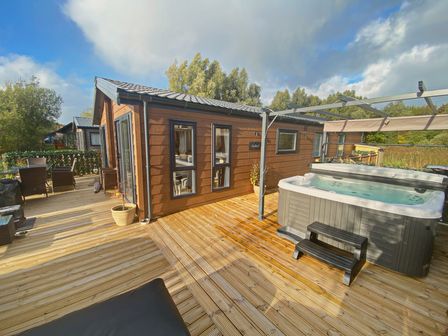 An outdoor wooden deck with a hot tub dining table chairs and a small house at Pine Lake View Coniston View 3 Carnforth