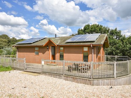 A wooden cabin with solar panels on the roof and a fenced wooden deck outside at The Hideaway in Eype