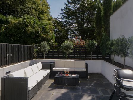 An outdoor patio with black wicker sofas with white cushions a coffee table and barbecue at Brompton Gardens in Torquay