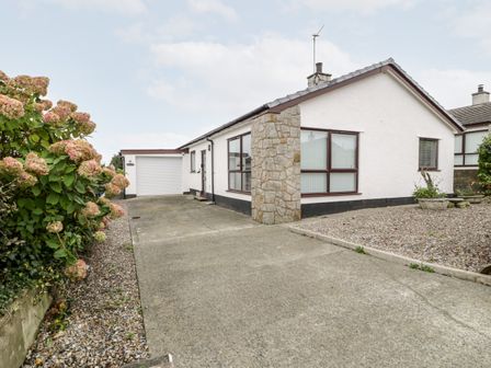 A single story white house with a garage driveway and gravel garden at Cae Teg in Niwbwrch newborough