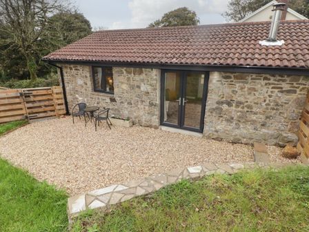 A stone building with a tiled roof and glass double doors opening to a gravel patio with outdoor table and chairs at The Stable in Amroth
