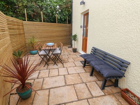 A patio area with a wooden table and chairs a bench with cushions and potted plants at The Loft @ Wisteria Cottage in Saundersfoot