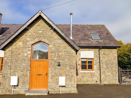 Stone house with wooden door and window under a pitched roof at School Lodge in Llandeilo