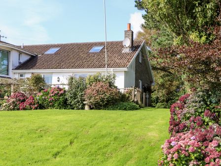A house with a sloped roof and skylight windows surrounded by green lawn and flowering bushes at Little Roskrow in Penryn near Falmouth