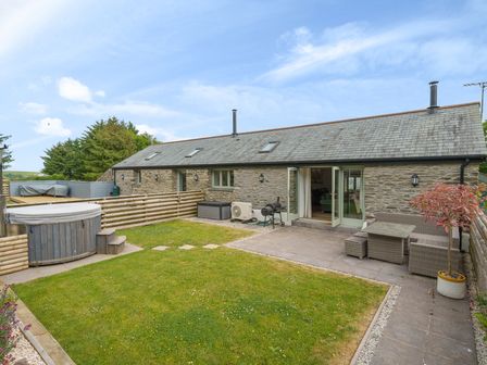 A stone house with a grassy backyard patio furniture and a hot tub at The Granary in Davidstow near Camelford