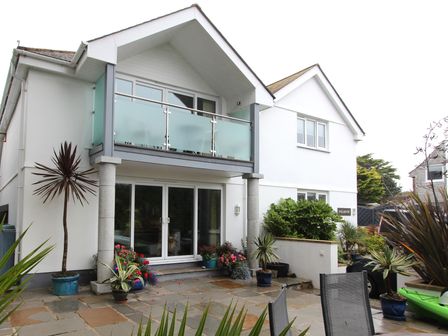 A white two-story house with balcony glass railing and potted plants at Polmoor Carbis Bay