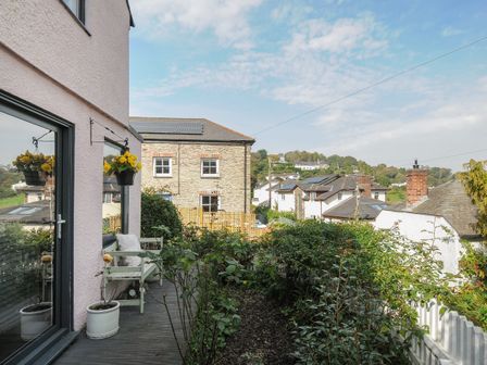 A small garden area with plants and flowers outside a house with a bench and hanging flower pot at Moon's Cottage in Fowey