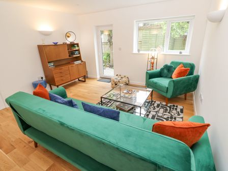 A living room with a green sofa and armchair with cushions a wooden cabinet a glass coffee table a patterned rug and a window at James Place in Falmouth