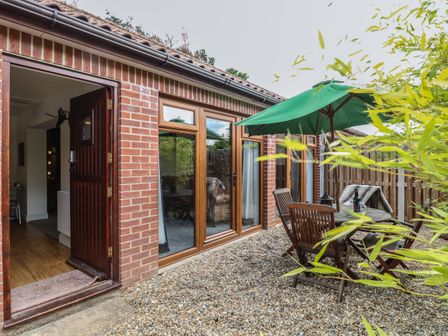 A patio area with wooden chairs and table under a green umbrella outside a brick house at The Bull Pen Rackheath near Norwich and the Norfolk Broads
