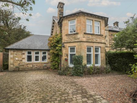 A stone house with multiple windows and a driveway with paving stones and gravel at St Aidans in Alnwick