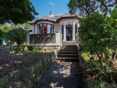 Exterior view of a house with stairs leading to the entrance surrounded by trees and plants at Penang in St Austell