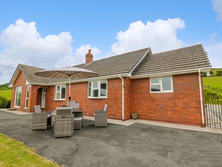 An outdoor patio with a table umbrella and chairs outside a brick house at Ashdale in Bwlch-y-sarnau near Rhayader